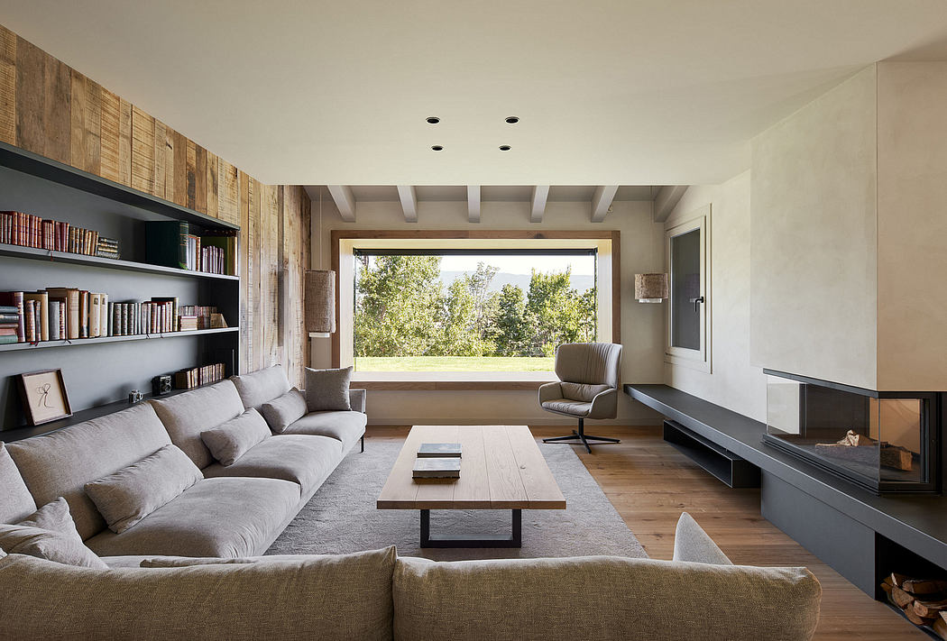 Minimalist, open-concept living room with wooden beams, built-in bookshelves, and large window framing the outdoor view.