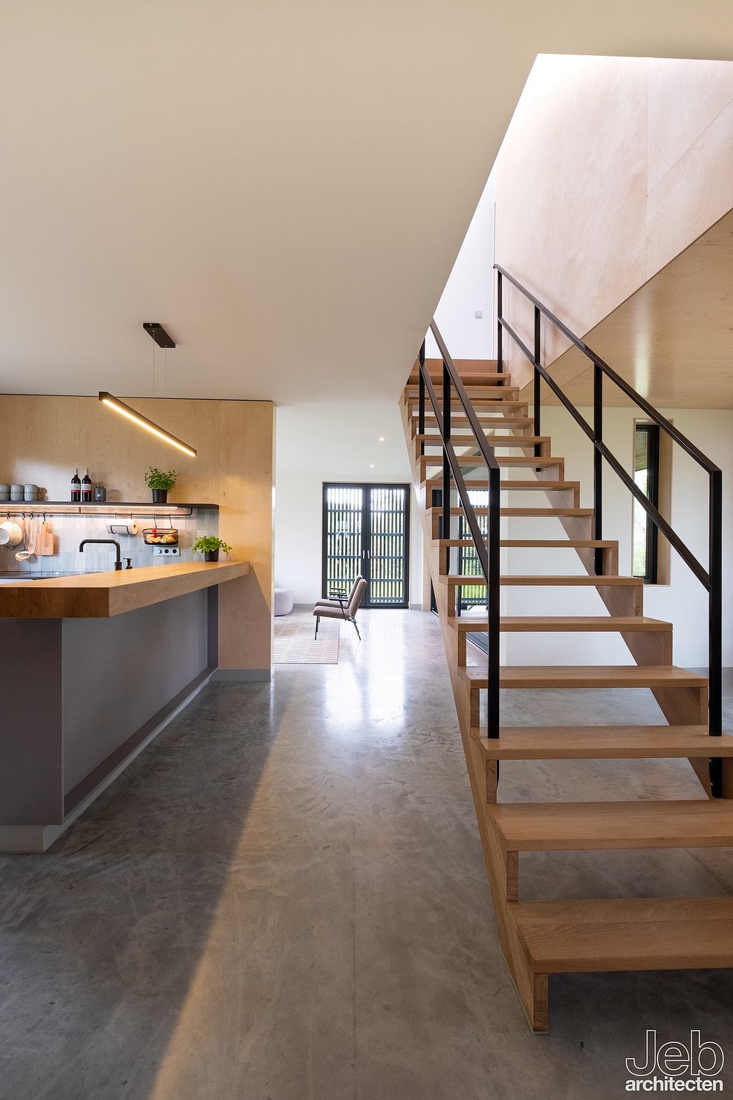 A modern, open-concept interior with a wooden staircase, minimalist kitchen, and natural light.