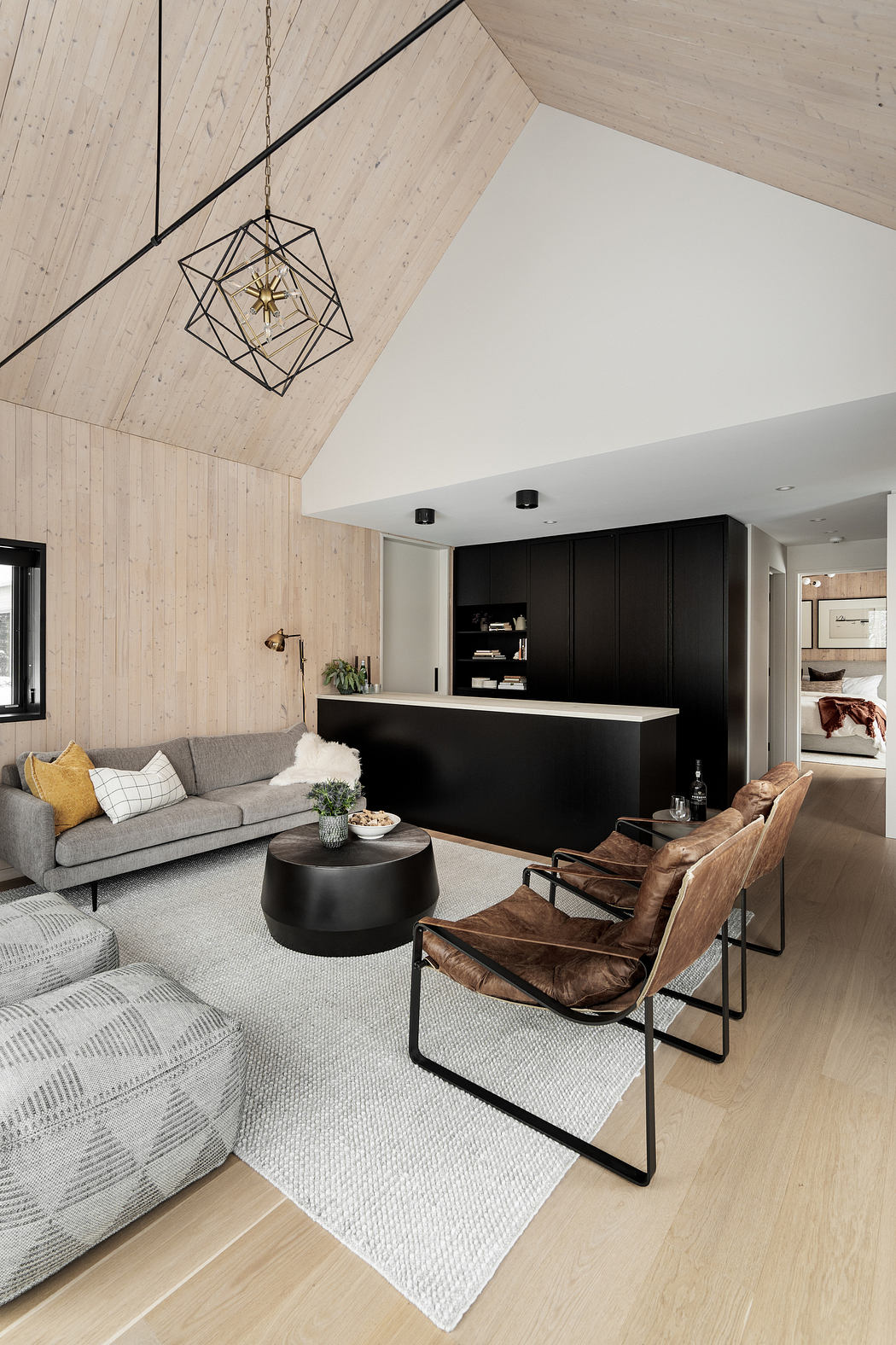 Sleek, modern living room with wooden vaulted ceiling, geometric lighting fixture, and dark cabinetry.