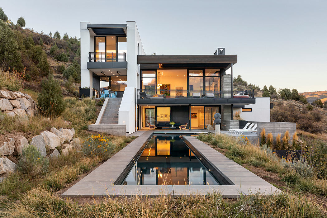 Modern hillside home with sleek, linear architecture, large windows, and a reflecting pool.