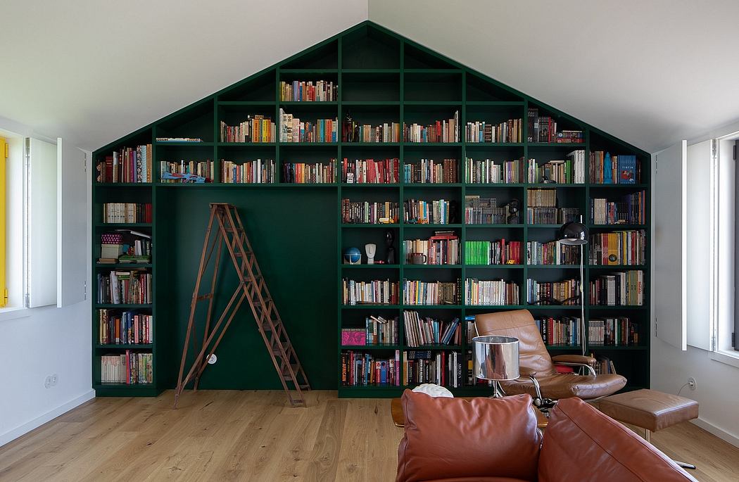 A cozy reading nook with a floor-to-ceiling bookshelf in a deep green hue, complemented by a leather armchair.