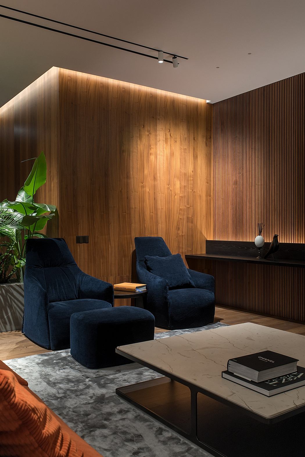 A modern lounge with plush navy armchairs, wood-paneled walls, and a sleek marble coffee table.