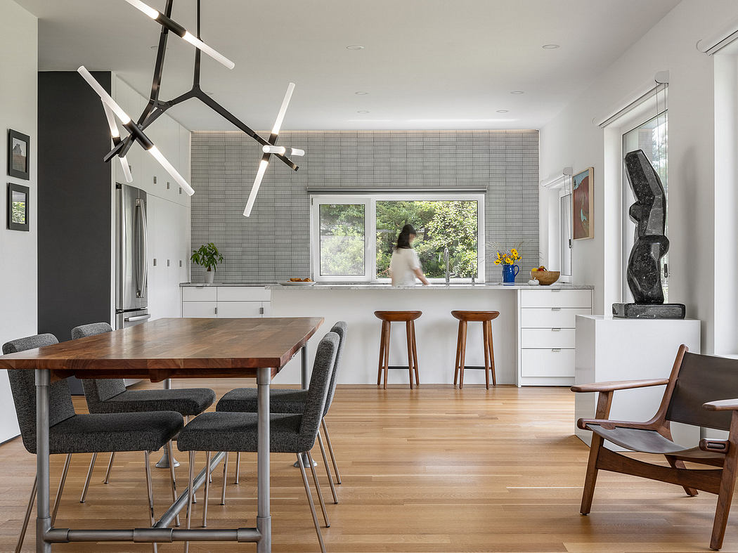 Bright, open-concept kitchen with wood dining table, modern lighting fixtures, and gray tiled walls.