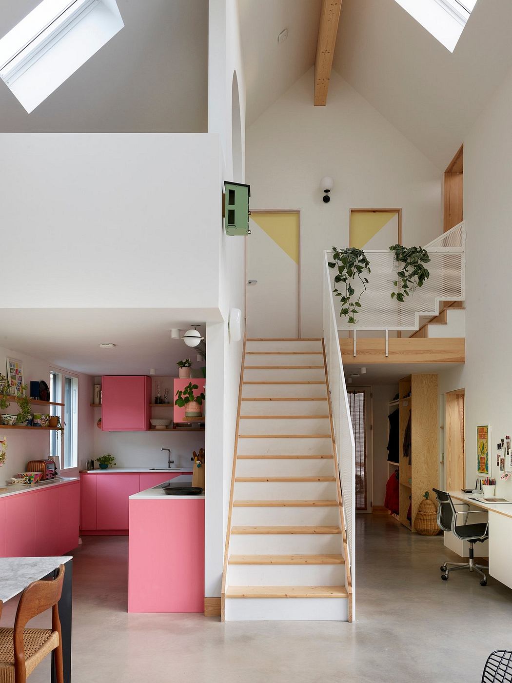 Bright, modern interior with pink kitchen cabinets, wooden stairs, and plants.