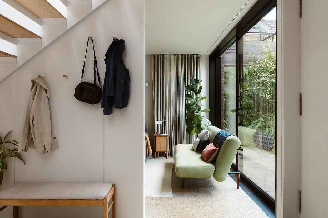Cozy entryway with wooden bench and hanging coats, leading to a serene living space with large windows.