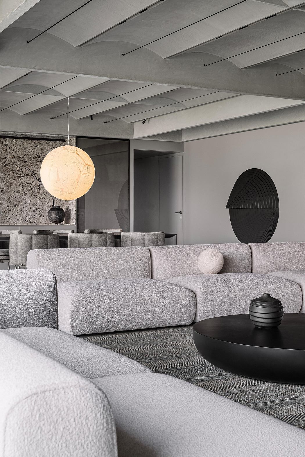 Modern minimalist living room with textured gray sofa, abstract wall art, and pendant lighting.