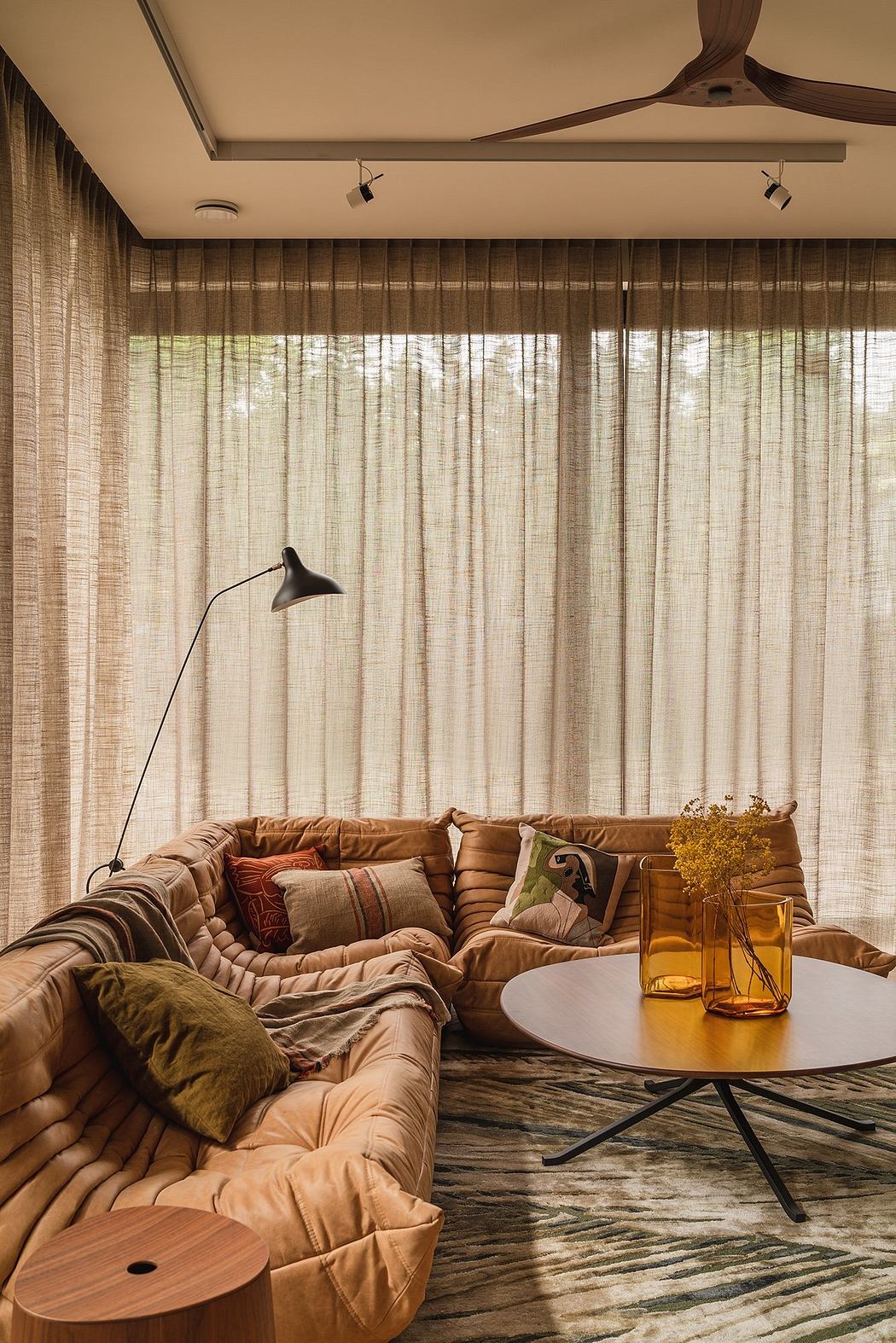 Cozy living room with wooden beams, layered curtains, patterned rug, and plush seating.