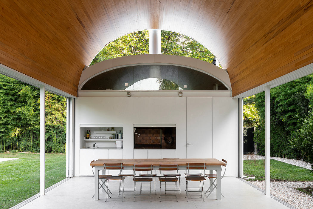 Elegant modern outdoor kitchen pavilion with wooden ceiling, open views, and a large dining table.