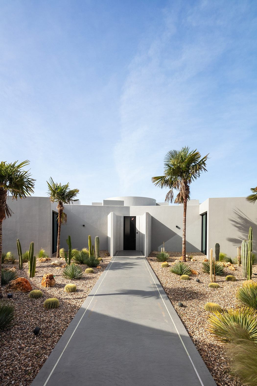Minimalist desert architecture with palm trees, cacti, and a concrete walkway.