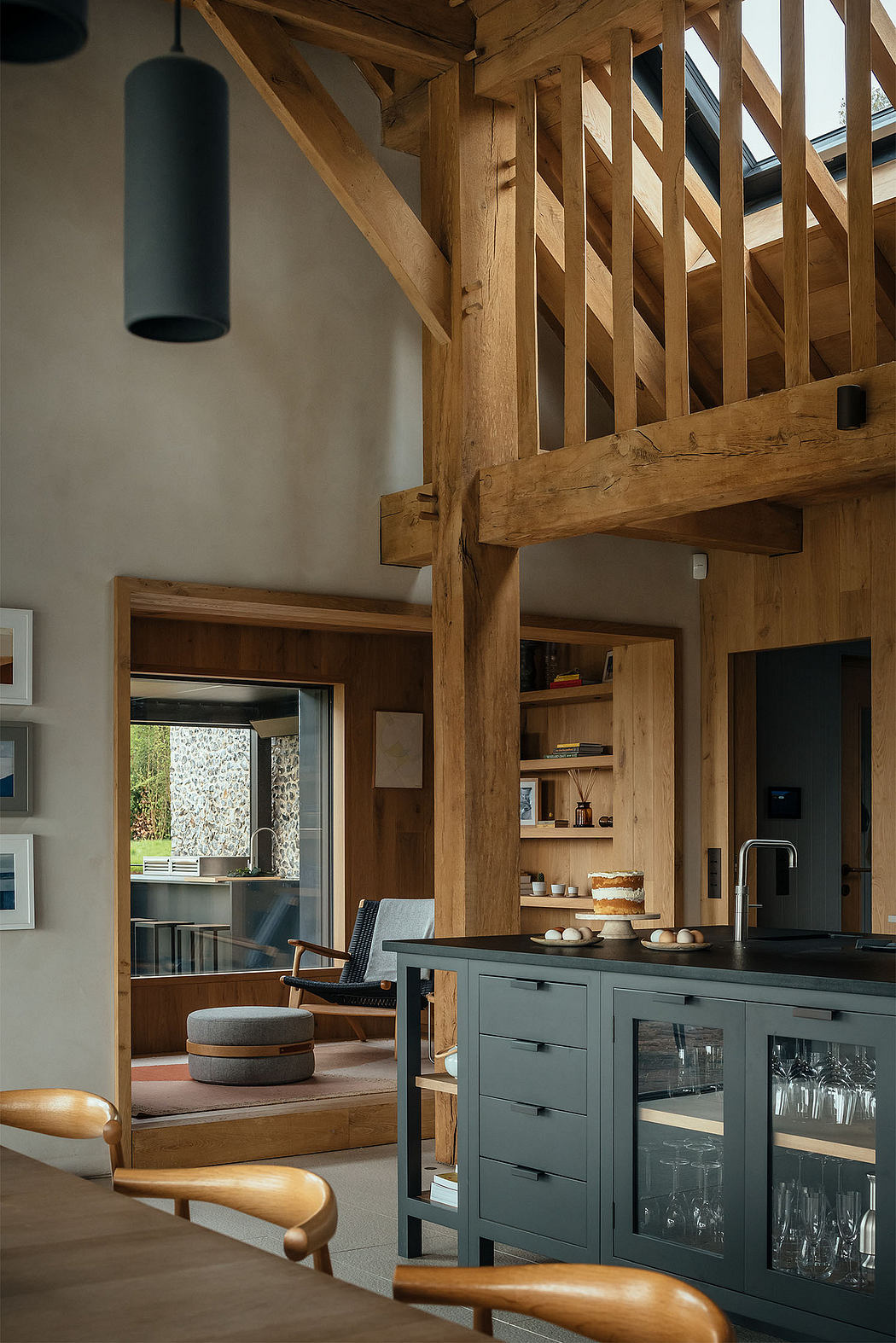 Modern rustic kitchen with exposed wooden beams, gray cabinets, and glass-fronted shelving.