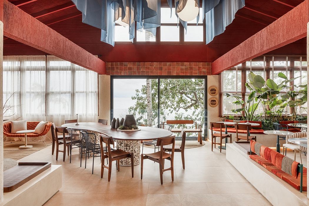 A modern, open-plan living space with earth-toned furnishings, high ceilings, and expansive windows showcasing lush outdoor greenery.