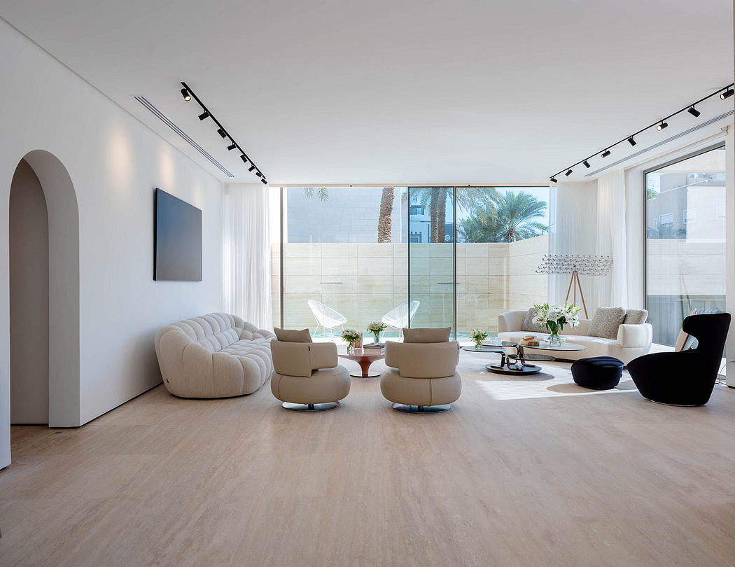 Spacious modern living room with sleek white sofas, armchairs, and large glass windows overlooking palm trees.