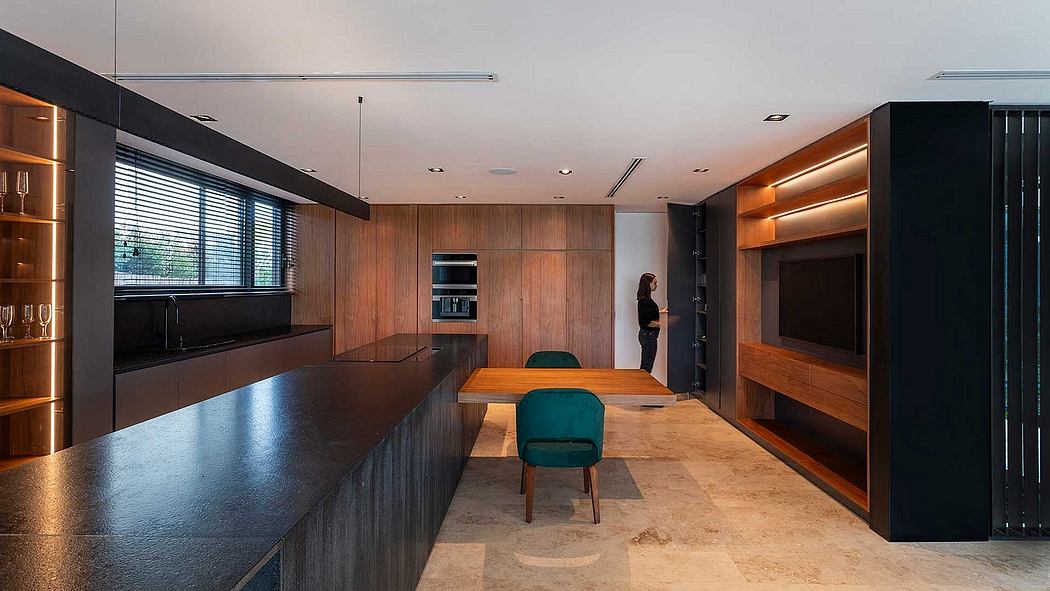 The image depicts a sleek, modern kitchen with wood paneled walls, a long wooden dining table, and a black kitchen island with integrated appliances.