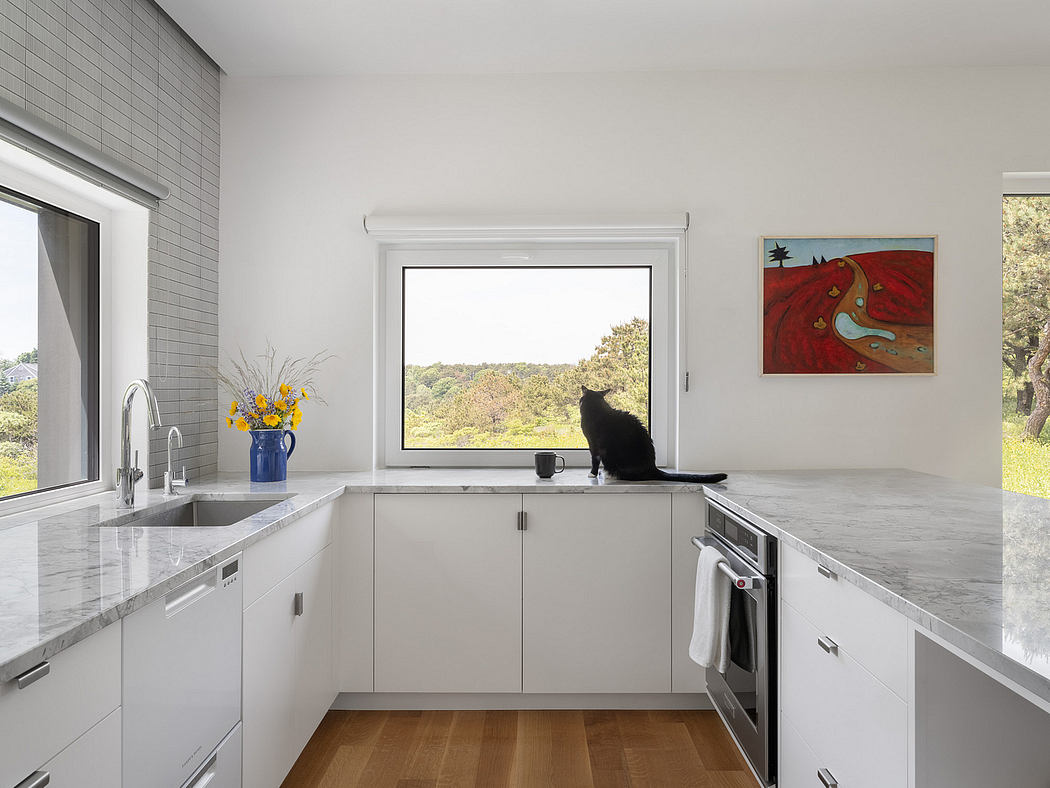A modern kitchen with sleek cabinetry, marble countertops, and large window overlooking nature.