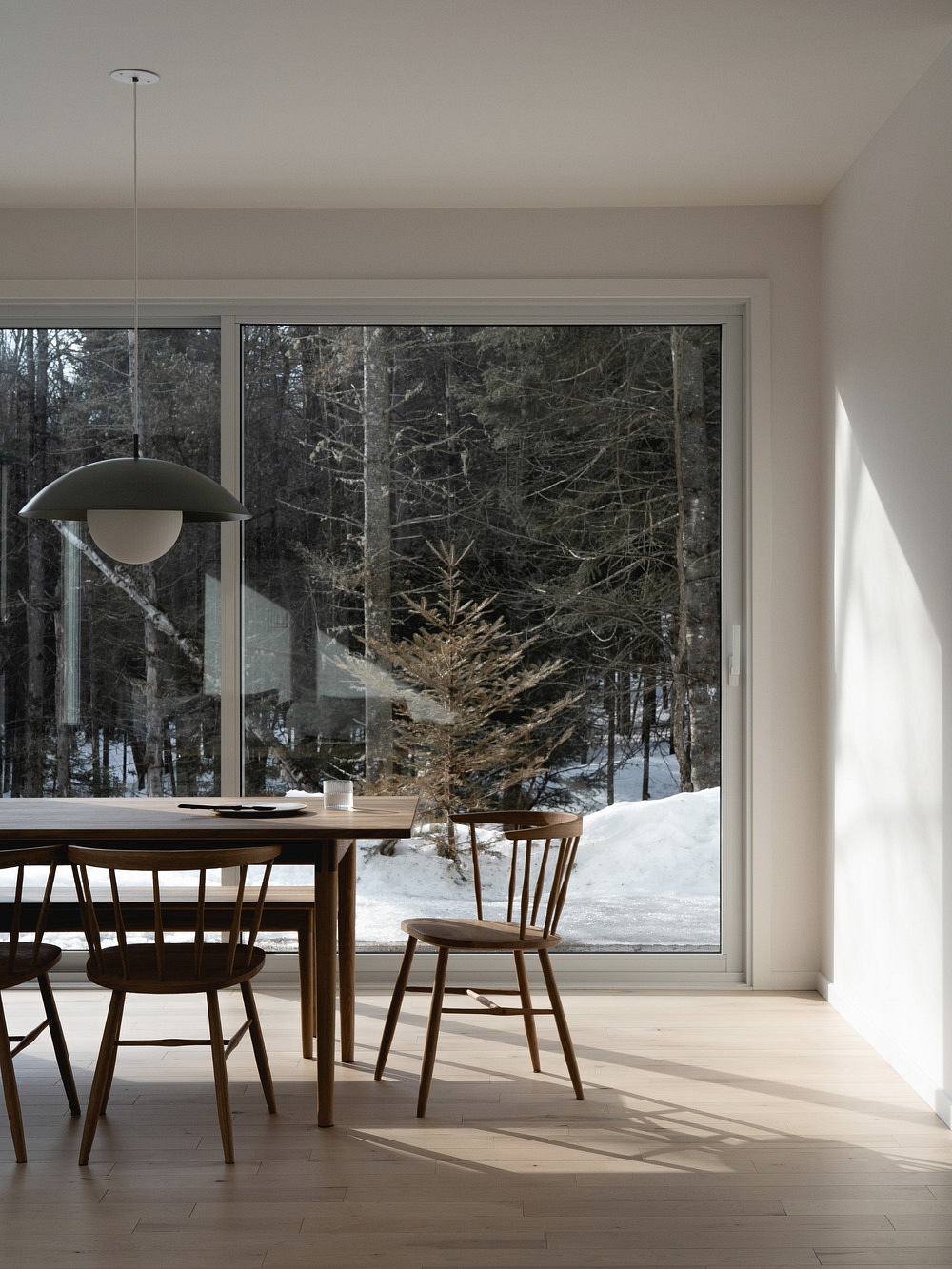 A cozy dining area with a large window overlooking a snowy forest, featuring a wooden table and chairs.