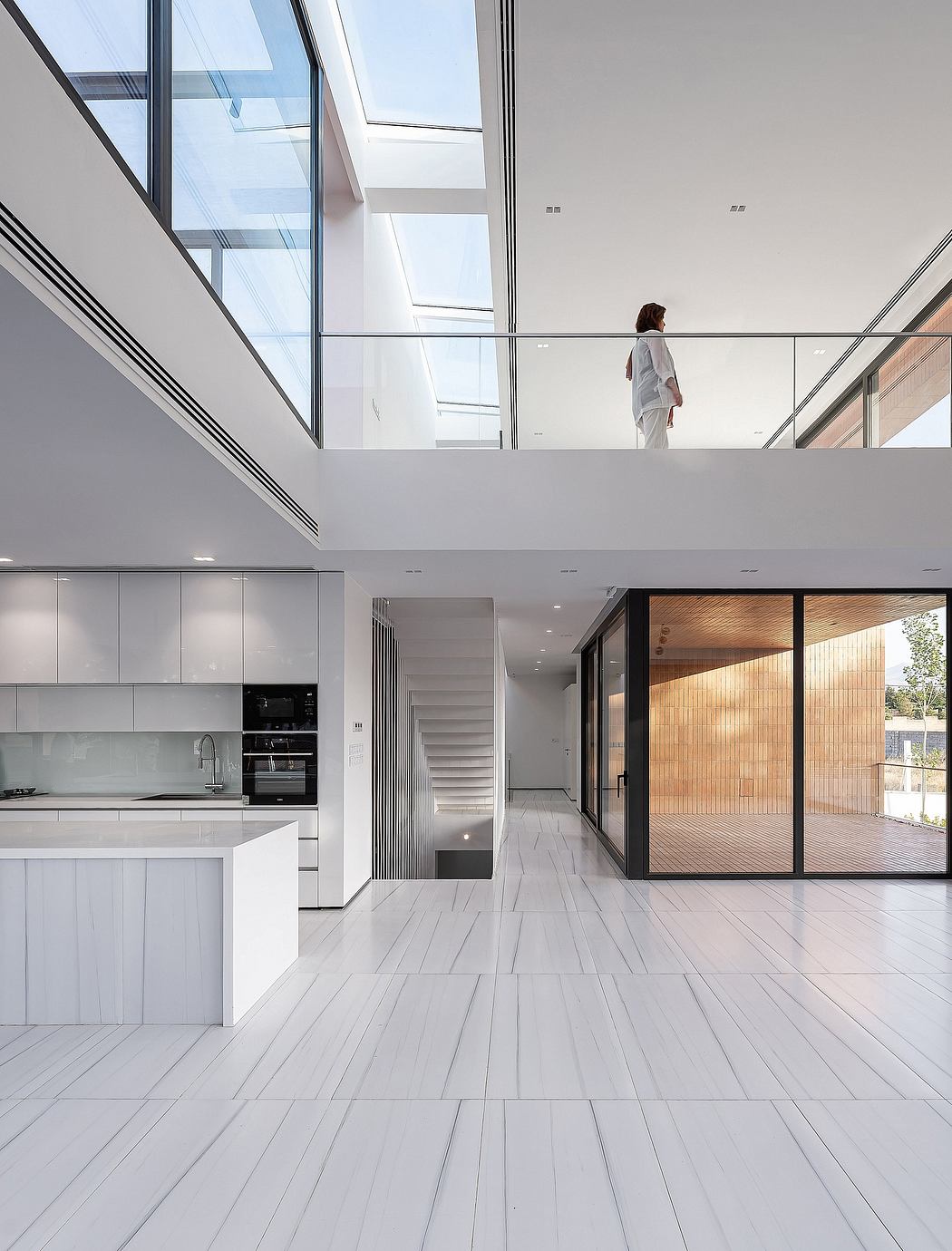 Spacious modern interior with sleek kitchen, glass walls, and a person visible in the distance.