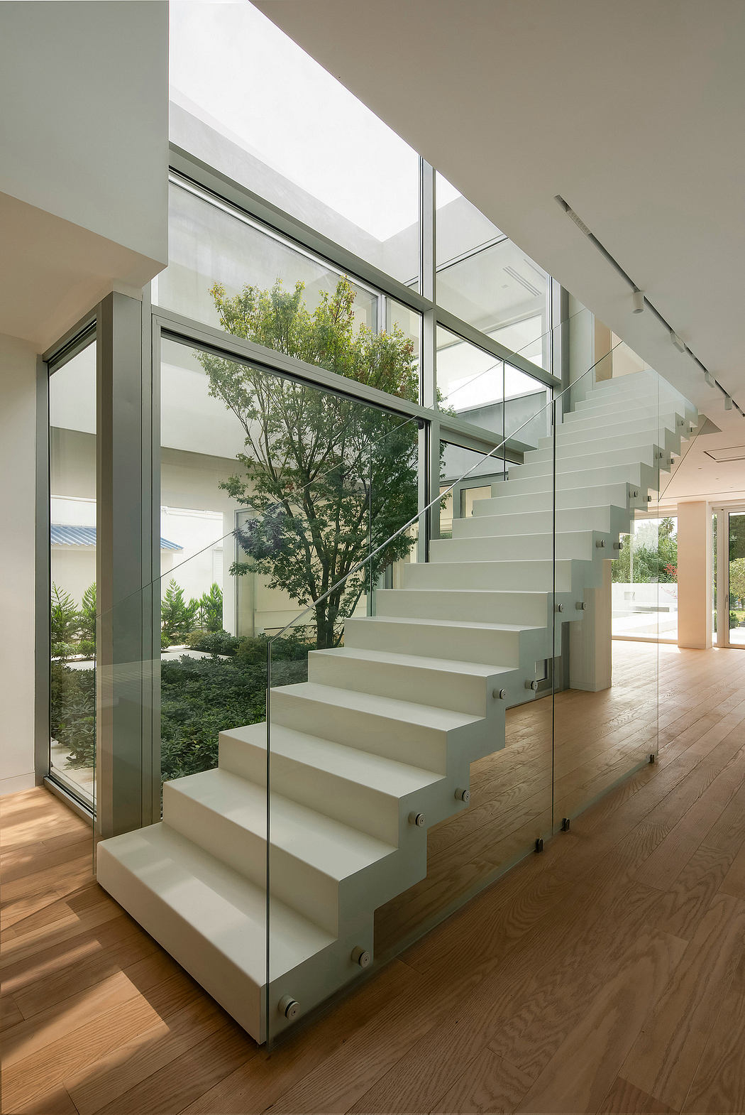 Modern staircase with glass panels and wooden floors, surrounded by nature views.