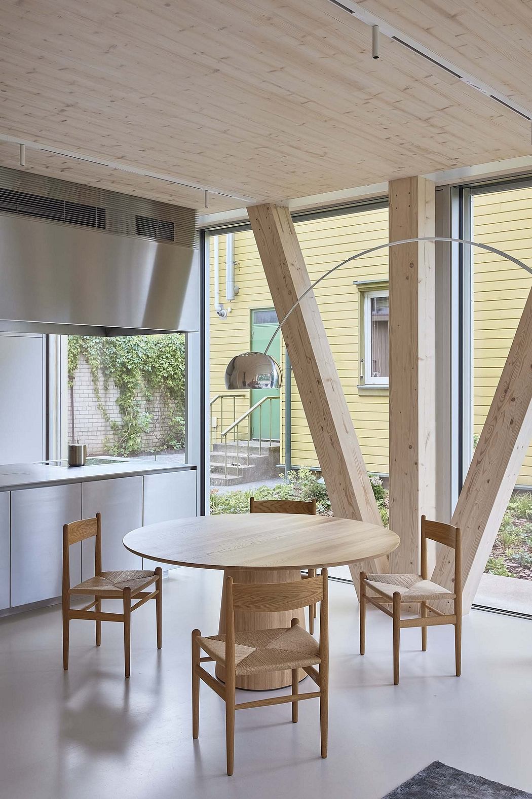A modern, minimalist interior with natural wood furnishings and large windows offering garden views.