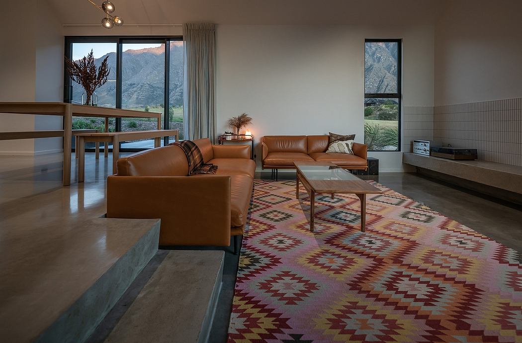 A modern living room with leather sofas, a patterned rug, and large windows framing a mountainous landscape.