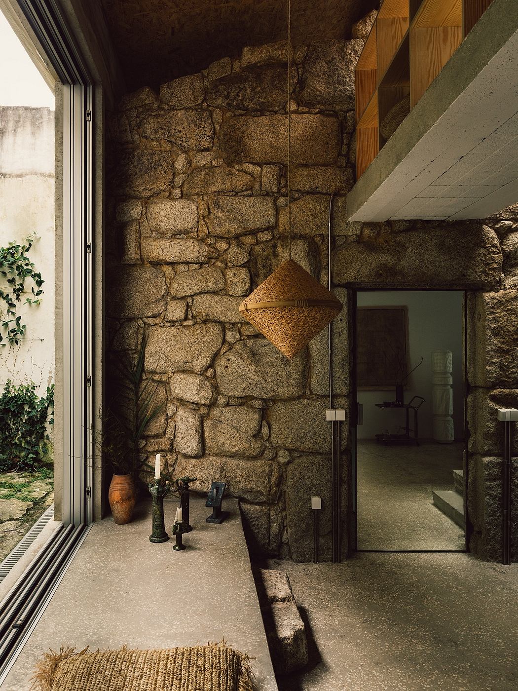 Rustic stone walls, minimalist furnishings, and a hanging light fixture create a cozy, modern atmosphere.