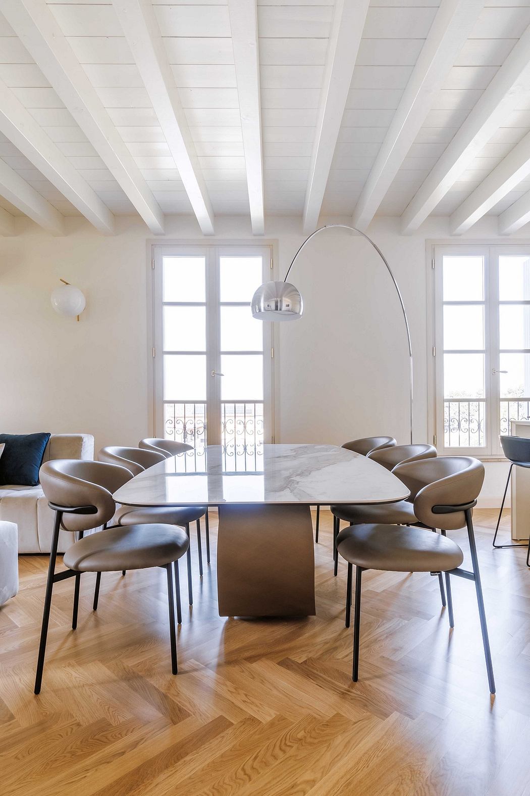 Sleek, modern dining area with marble-topped table, curved leather chairs, and arched windows.