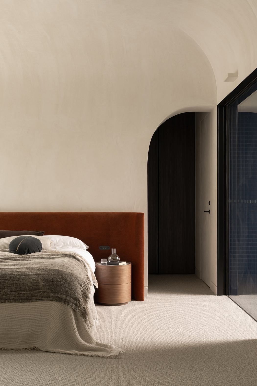 Minimalist bedroom with curved brick wall, wooden bedframe, and neutral color palette.