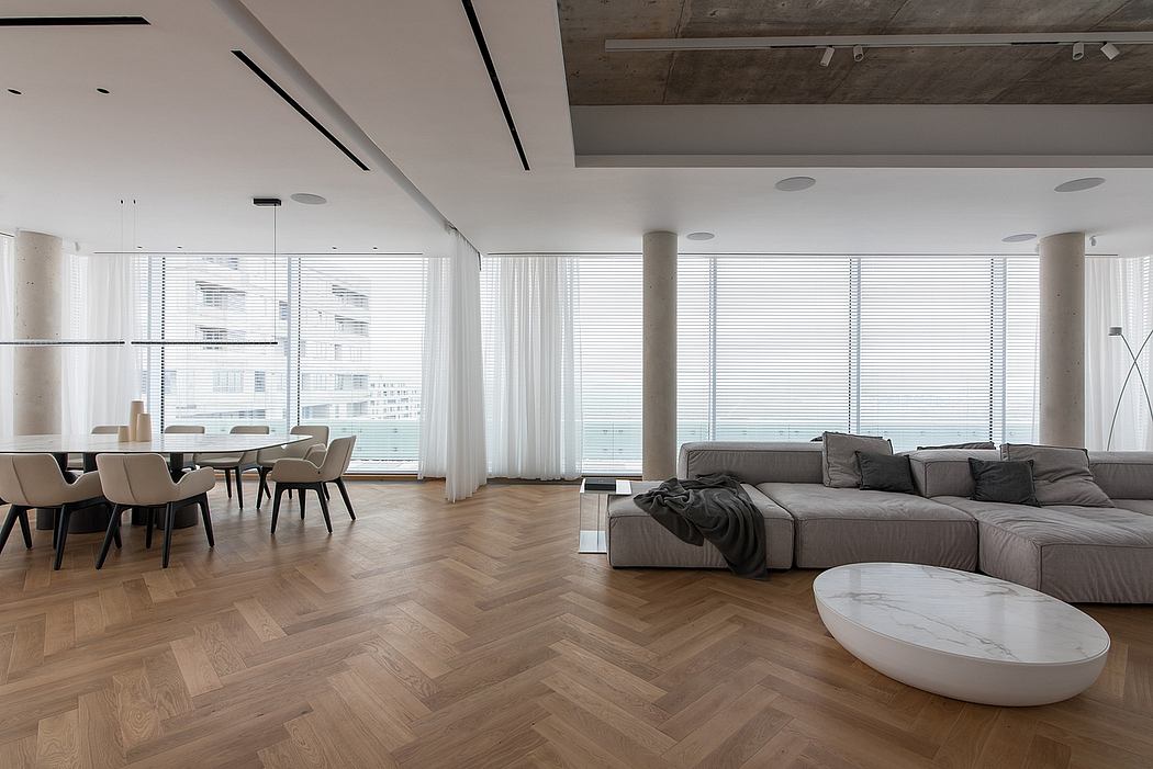 Spacious open-concept living area with modern furniture, herringbone wood flooring, and large windows.