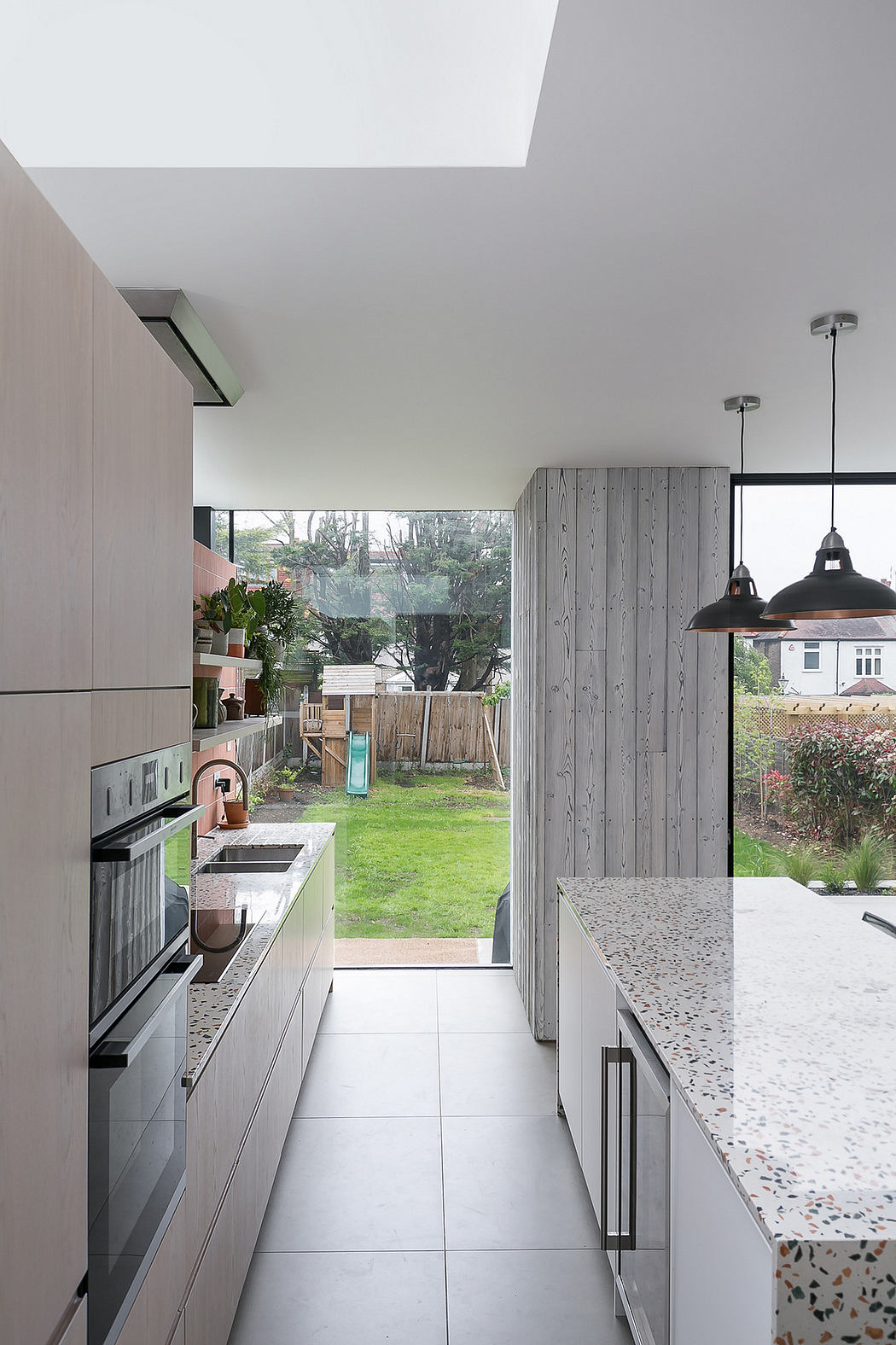 Modern kitchen with sleek gray cabinets, pendant lighting, and a view of the lush outdoor garden.