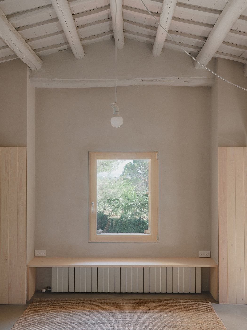 A minimalist interior with wooden beams, a window overlooking greenery, and a built-in bench.
