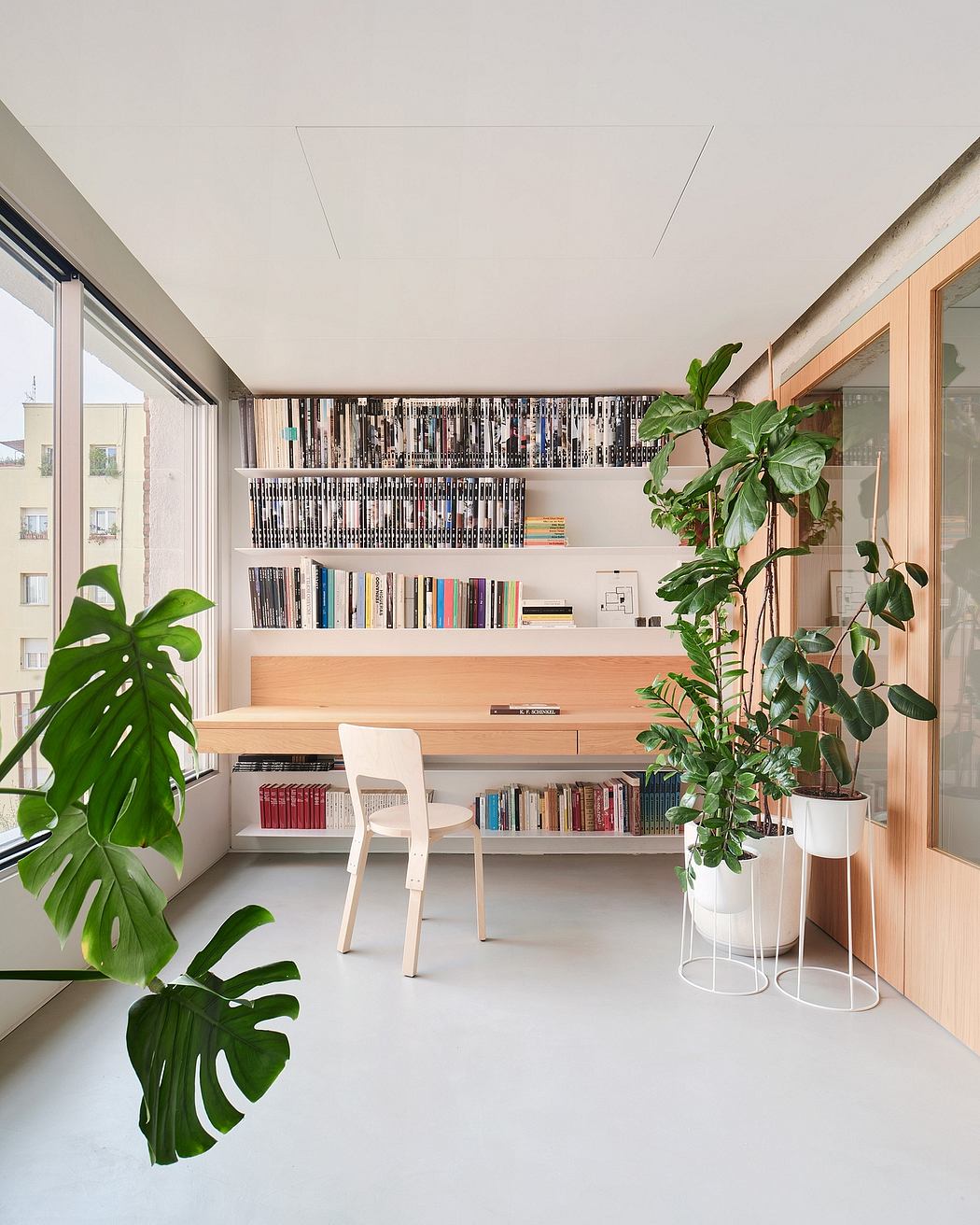 Cozy home workspace with ample bookshelves, potted plants, and a sleek wooden desk.