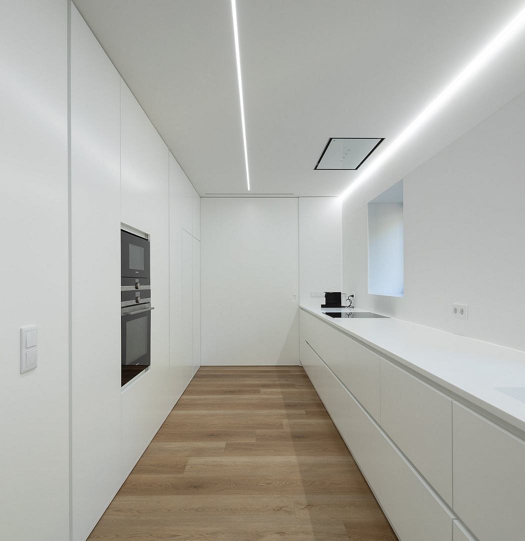 A sleek, minimalist kitchen with white cabinetry, wood flooring, and recessed lighting.