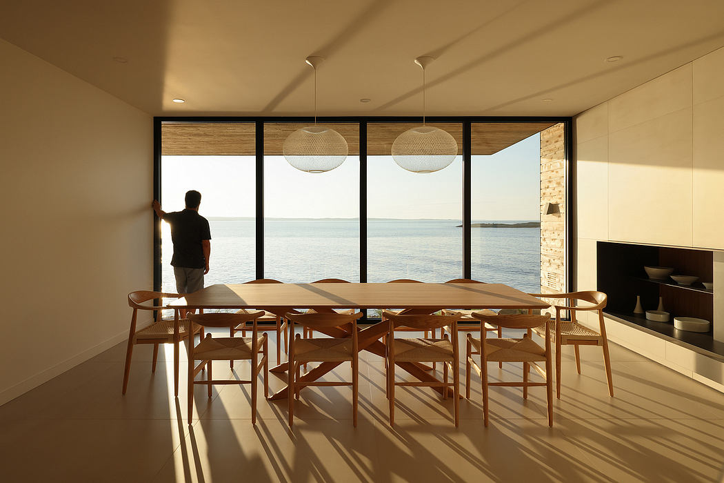 Spacious dining area with large windows overlooking a tranquil body of water, modern lighting, and a wooden table with chairs.