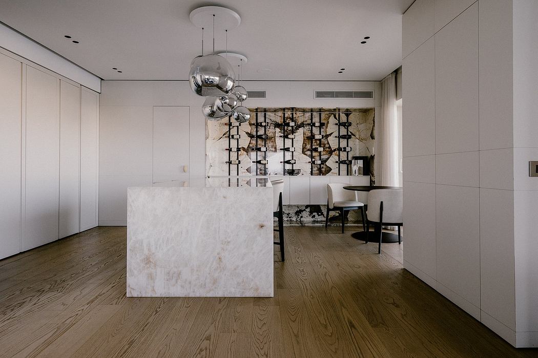 A modern, minimalist kitchen with a large white marble island, sleek pendant lights, and a bold abstract artwork.