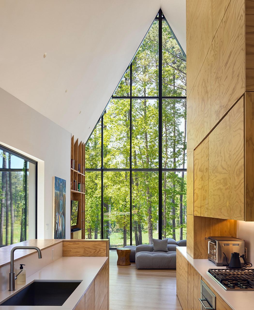 Large triangular window frames lush forest views in this modern, wood-accented kitchen.