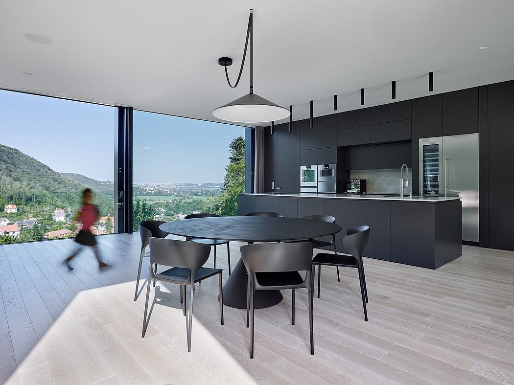 Modern kitchen-dining area with sleek black cabinetry, large windows offering scenic views.