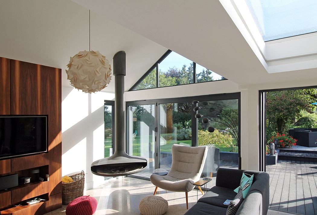 Modern living room with vaulted ceiling, fireplace, and large windows overlooking a garden.