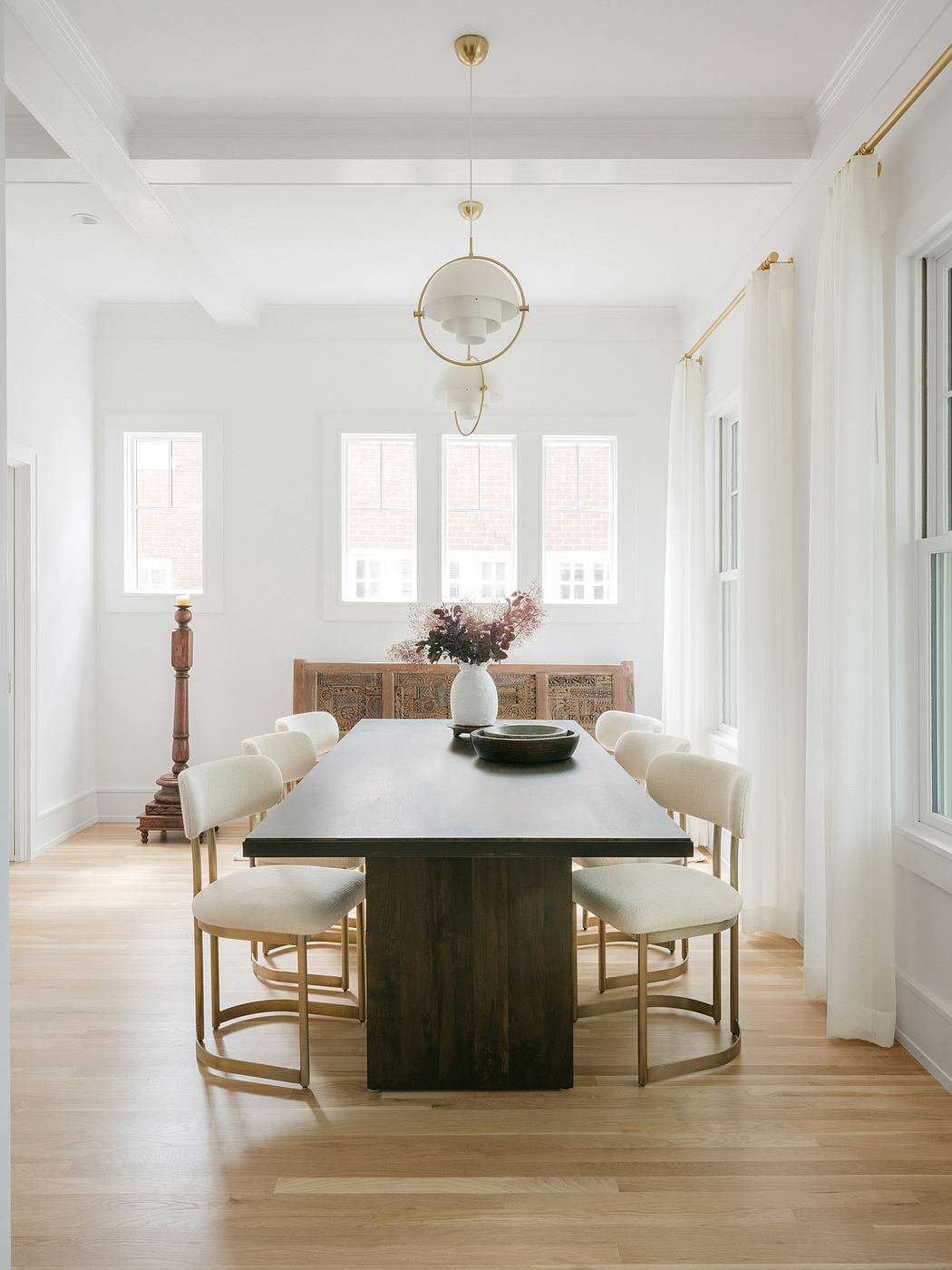 A bright, airy dining room with tall windows, a large wooden table, and elegant chairs.