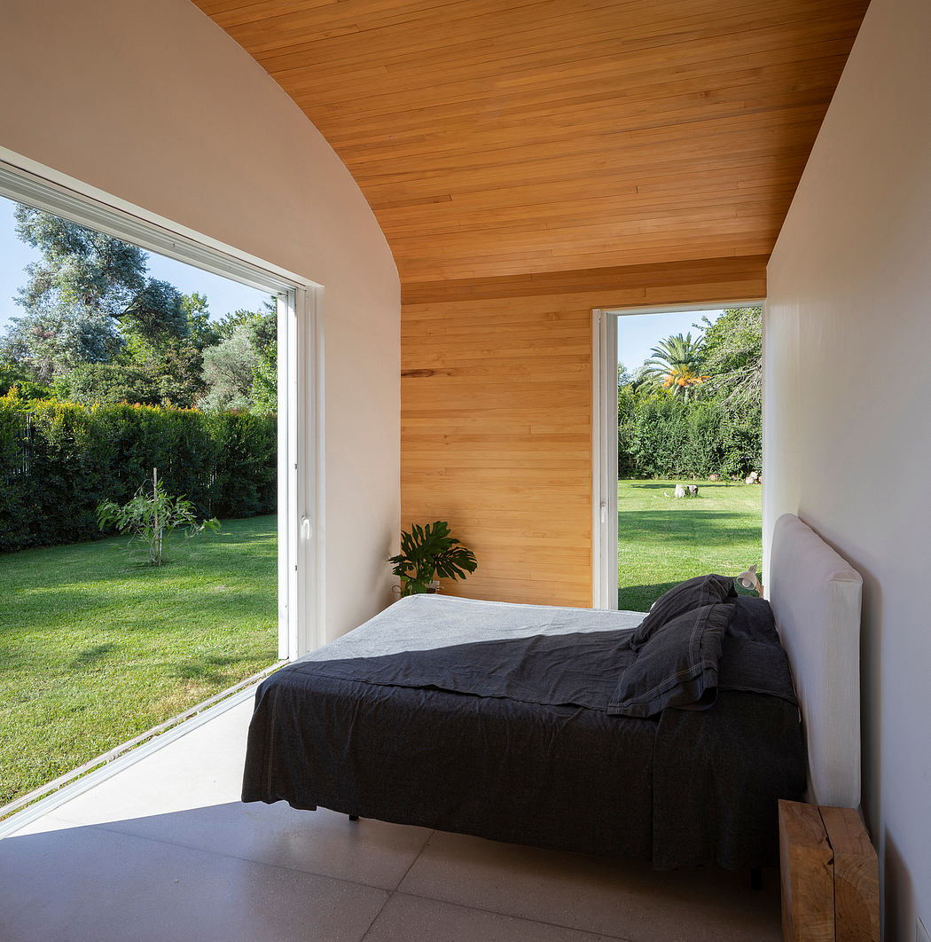 A cozy bedroom with a wooden ceiling, large windows overlooking a lush garden.