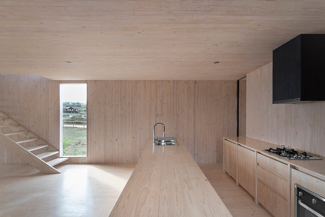 A minimalist wooden kitchen with a long counter and a view to the outdoors.