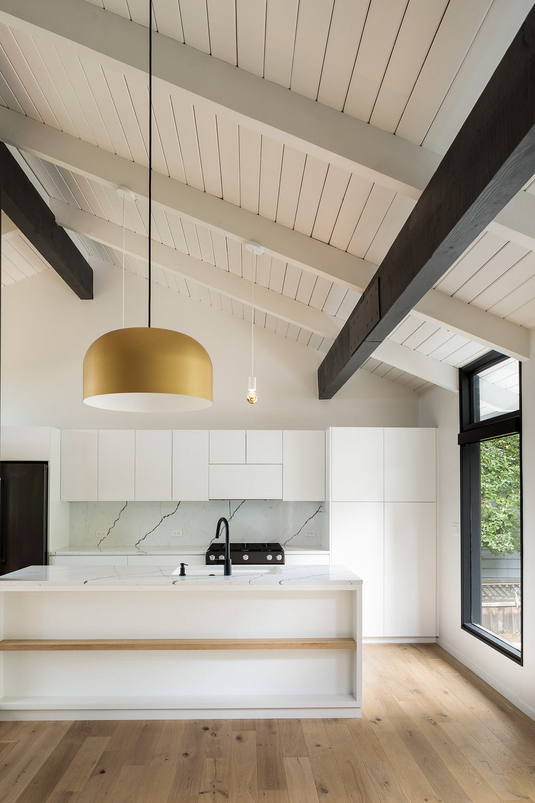Minimalist kitchen with wooden beams, white cabinetry, and a sleek gold pendant light.