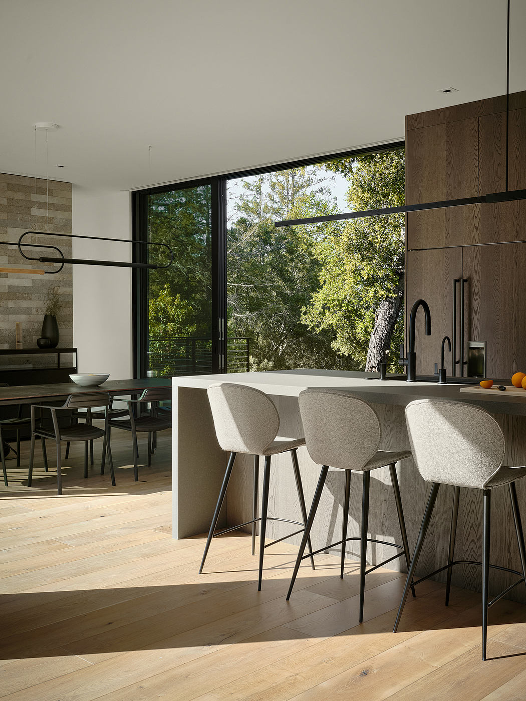 Sleek, modern kitchen with floor-to-ceiling windows overlooking lush greenery and a minimalist dining area.