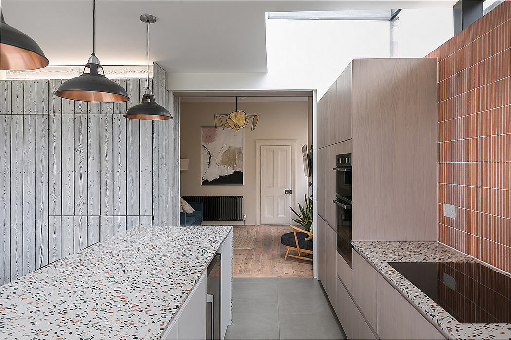 Modern kitchen with industrial-style lighting, terrazzo countertops, and warm wood cabinetry.