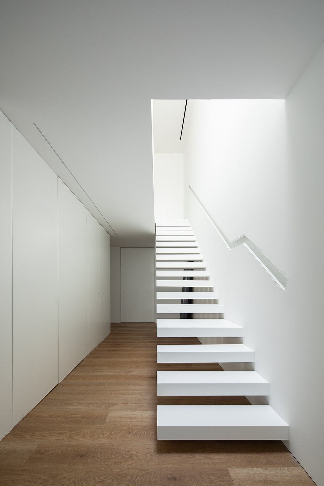 A minimalist staircase with clean, white steps leading up to a bright, open space.