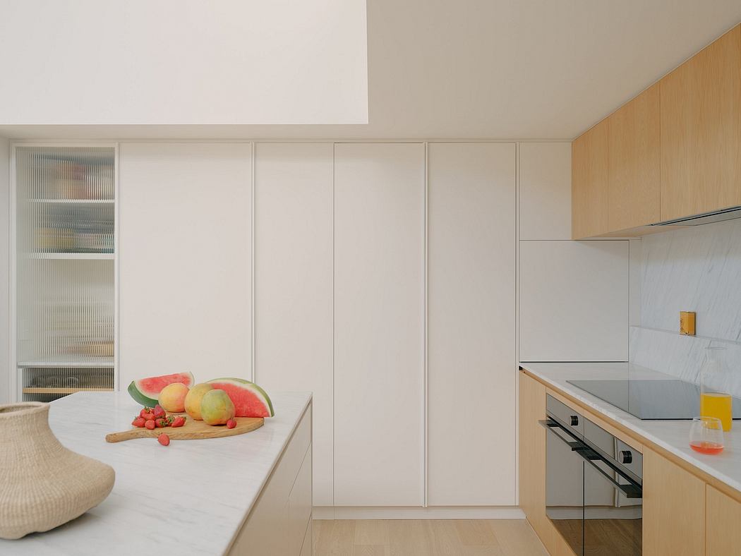 Minimalist kitchen with sleek white cabinets, wooden accents, and an array of fresh fruits.