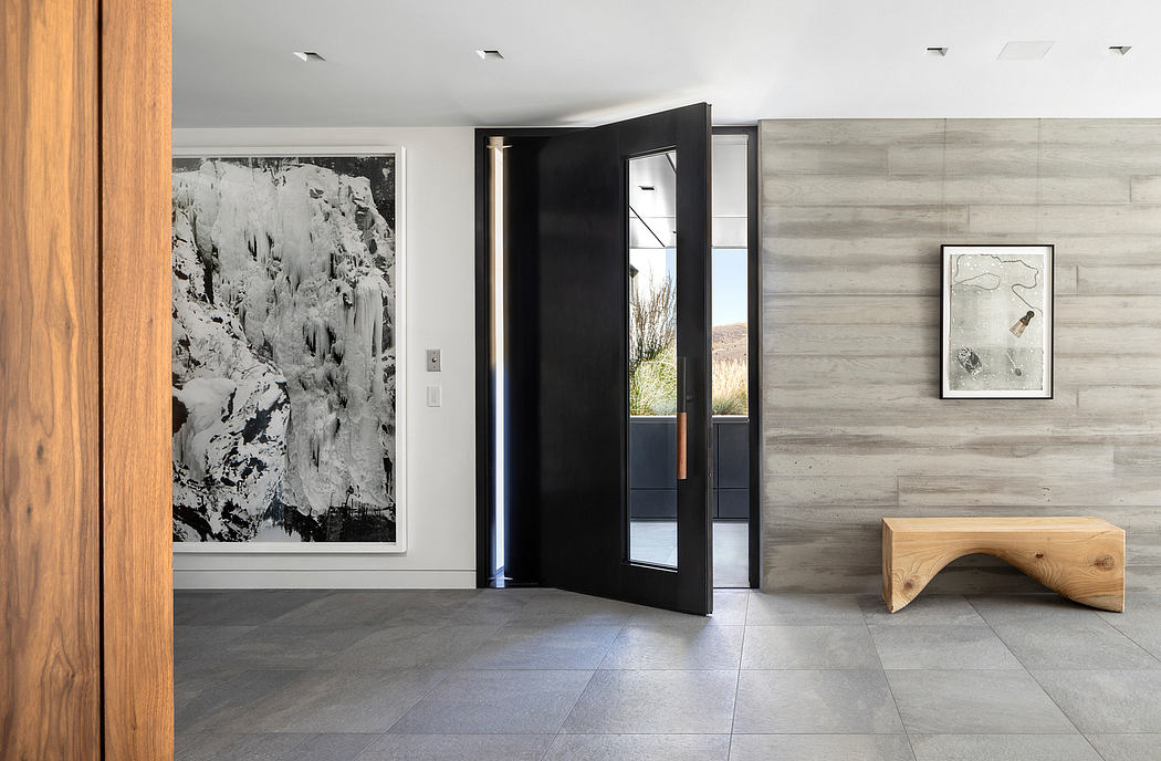 Monochromatic modern entryway with large black pivot door, wood-paneled walls, and minimalist bench.