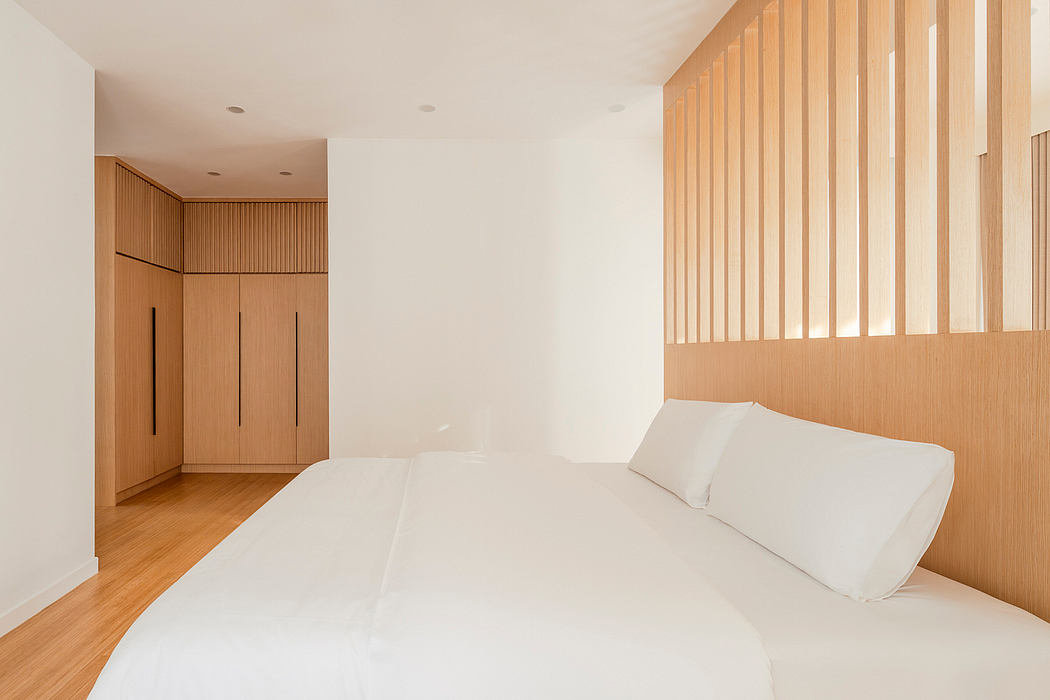Minimalist bedroom with clean lines, warm wood paneling, and a plush white bed.