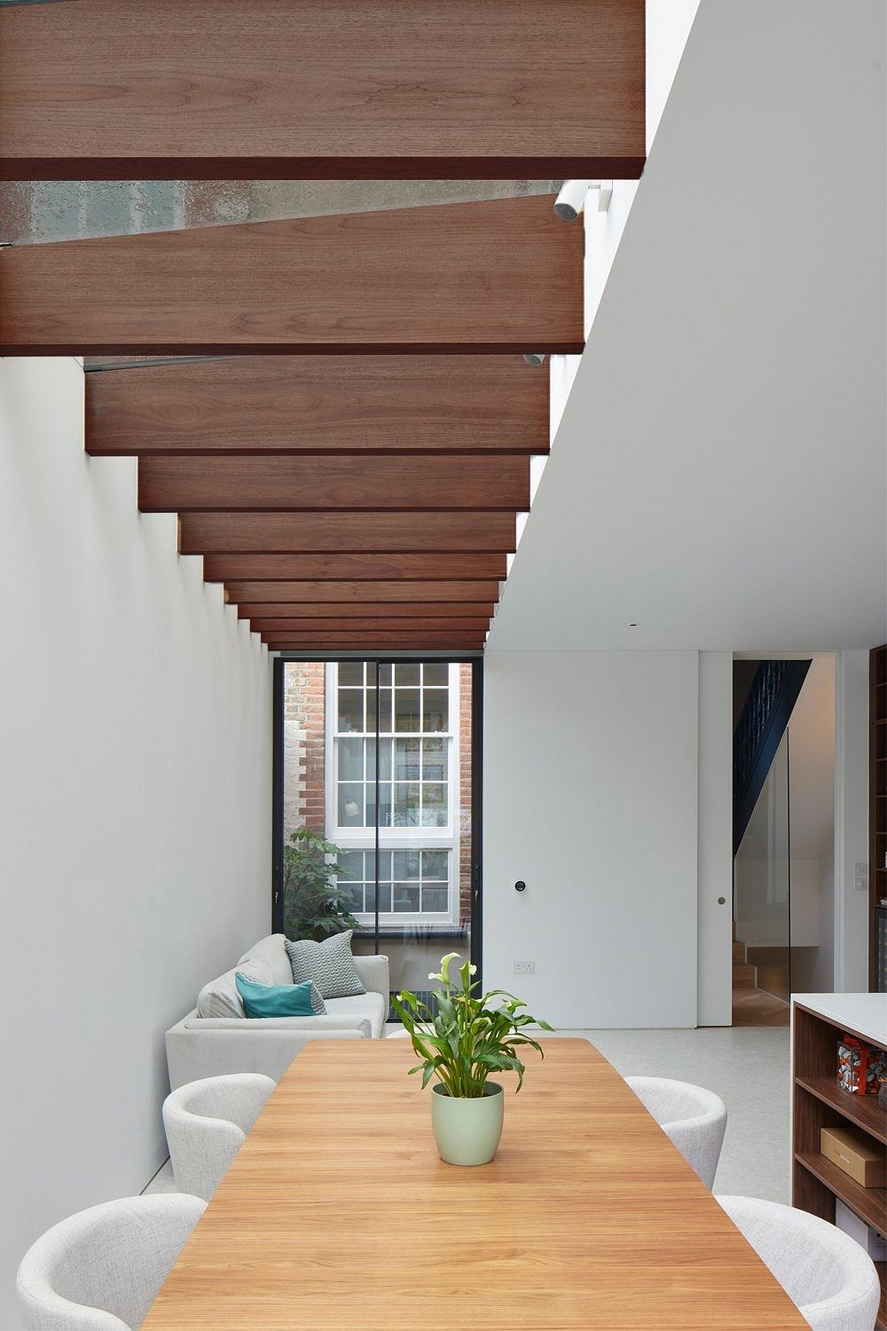 Minimalist interior with exposed wooden beams and large window overlooking brick wall.