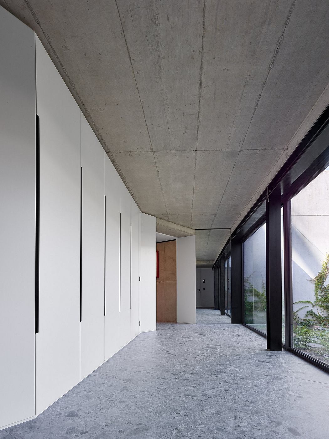 Minimalist interior with concrete ceiling, floor, and wall paneling; glass doors.