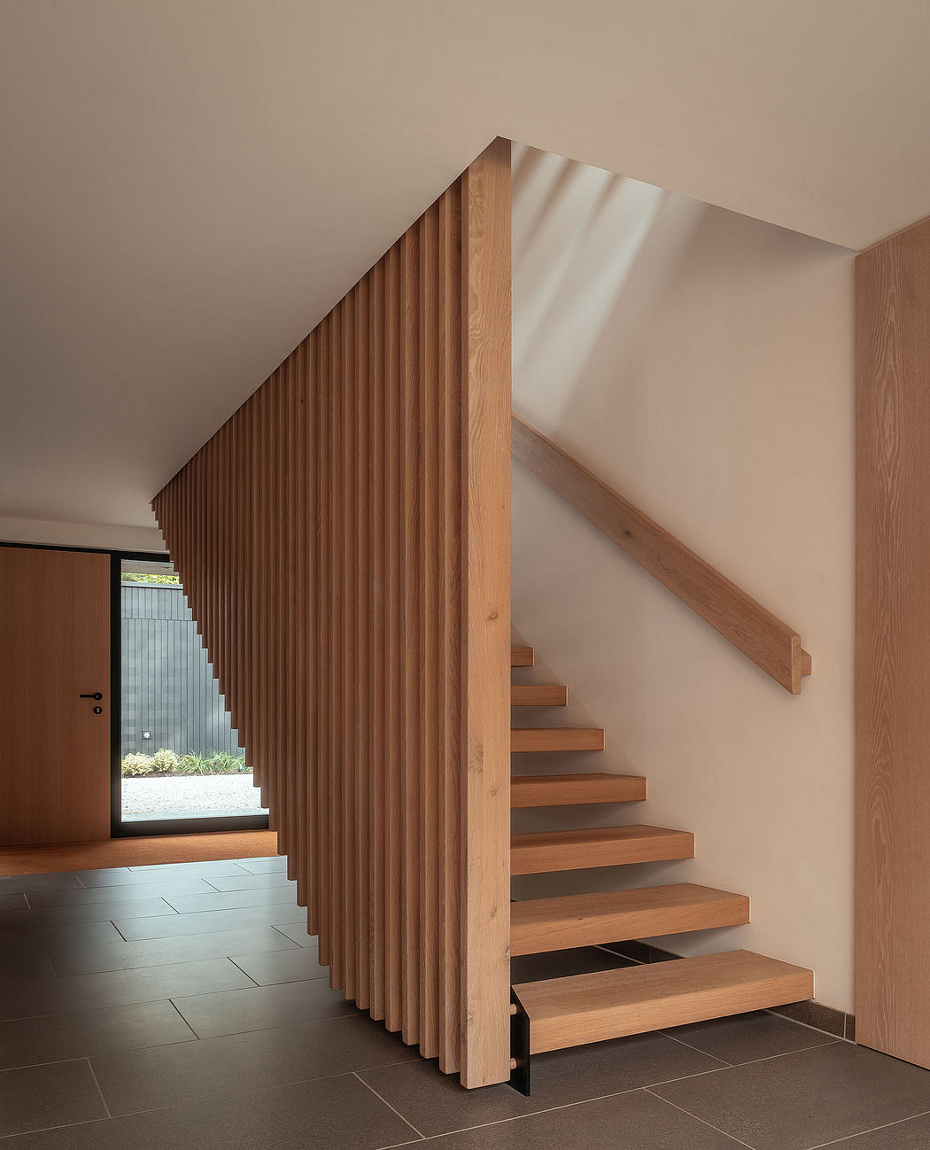 Warm-toned wooden staircase with vertical slat wall feature in modern entryway.
