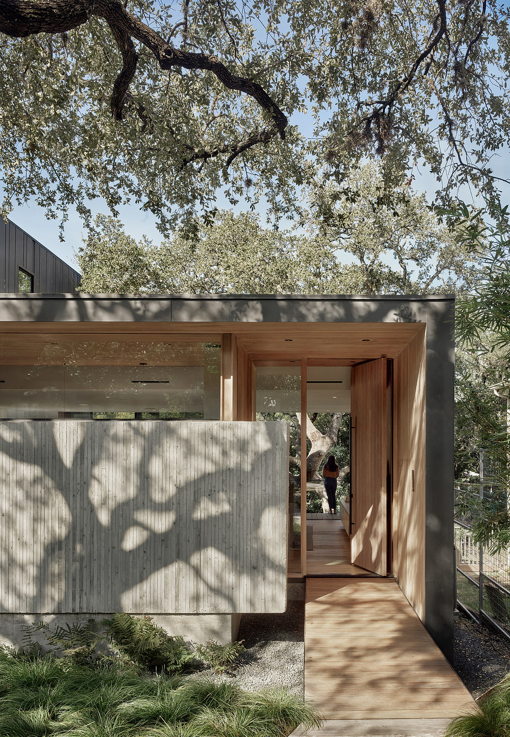 A modern, wood-framed house with a shaded entryway and lush, verdant surroundings.